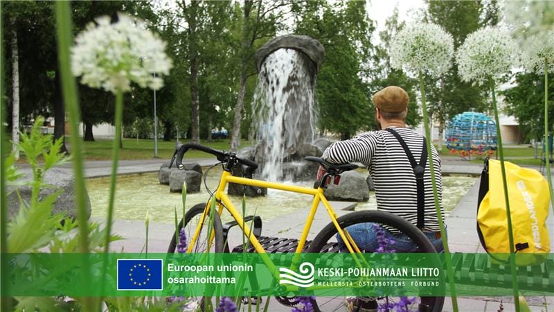 Pyöräilijä istuu puiston penkillä